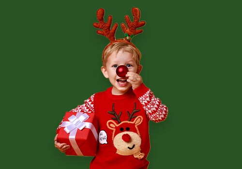 Kind mit Rentiergeweih hält Weihnachtsgeschenk und lächelt